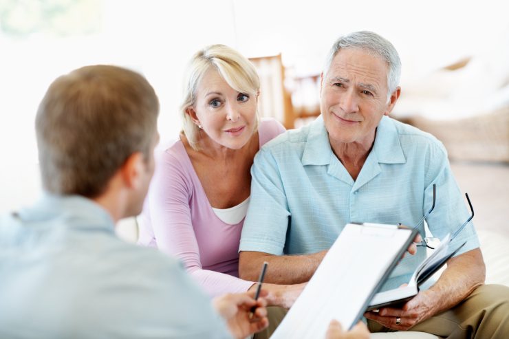 pensionati sorridenti di fronte a impiegato con documento in mano