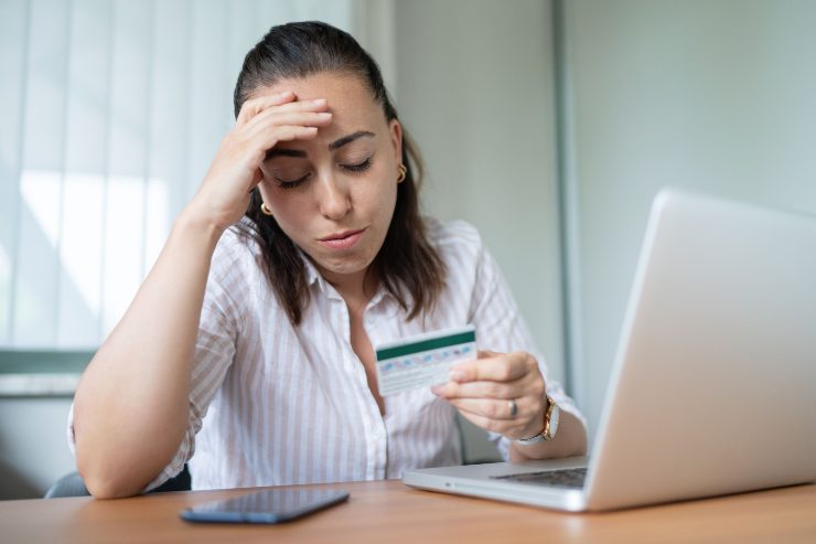 Ragazza giovane con una carta di credito in mano davanti al computer