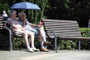 Coppia di anziani seduti su panchina che si proteggono dal sole con un ombrello