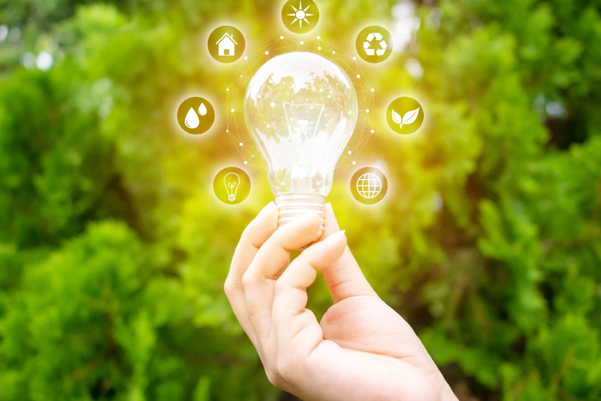 mano femminile tiene in mano una lampadina e intorno simboli energia
