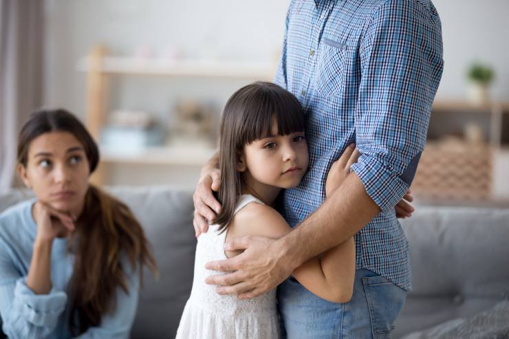 bambina trsite abbraccia papà e sullo sfondo la mamma guarda
