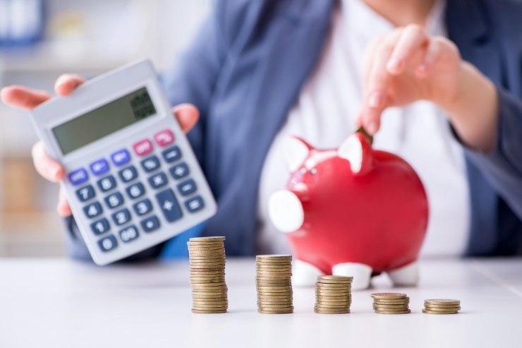 donna con calcolatrice in mano mette monete nel salvadanaio